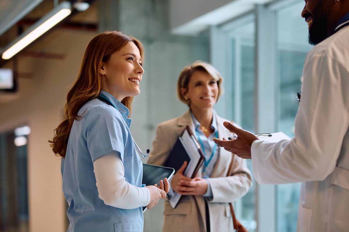 Doctor and nurse speaking with a healthcare business representative in a clinic hallway